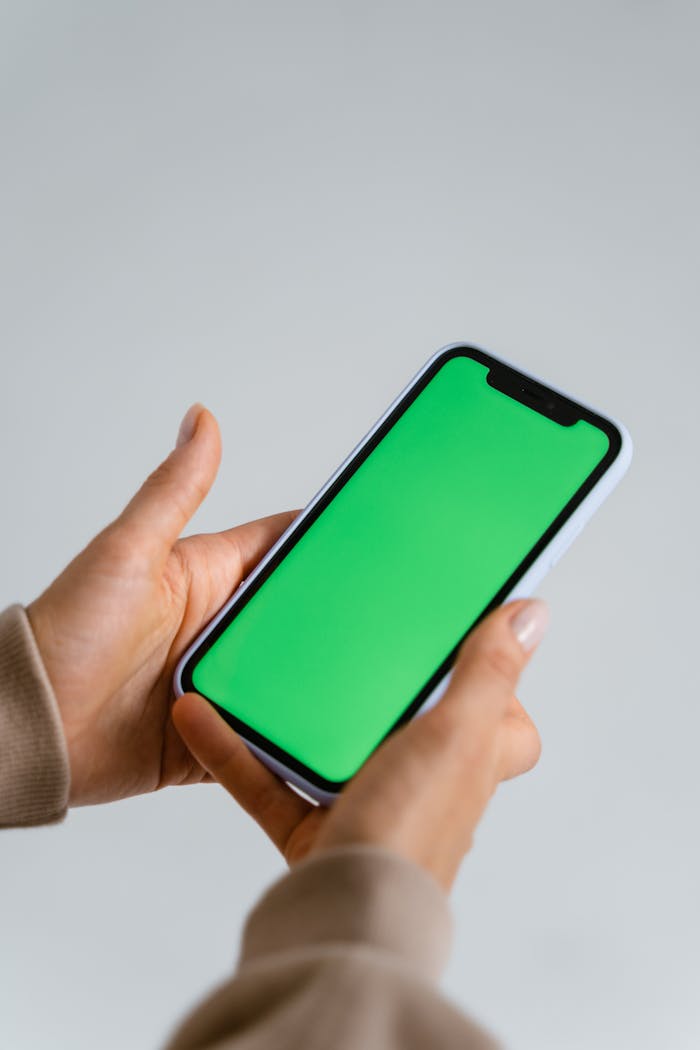 Hands holding a smartphone with a green screen, ideal for mockups and tech designs.